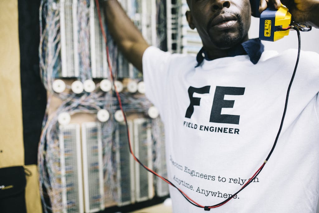 Crop concentrated African American field engineer in white shirt standing near panelboard with handset and looking away